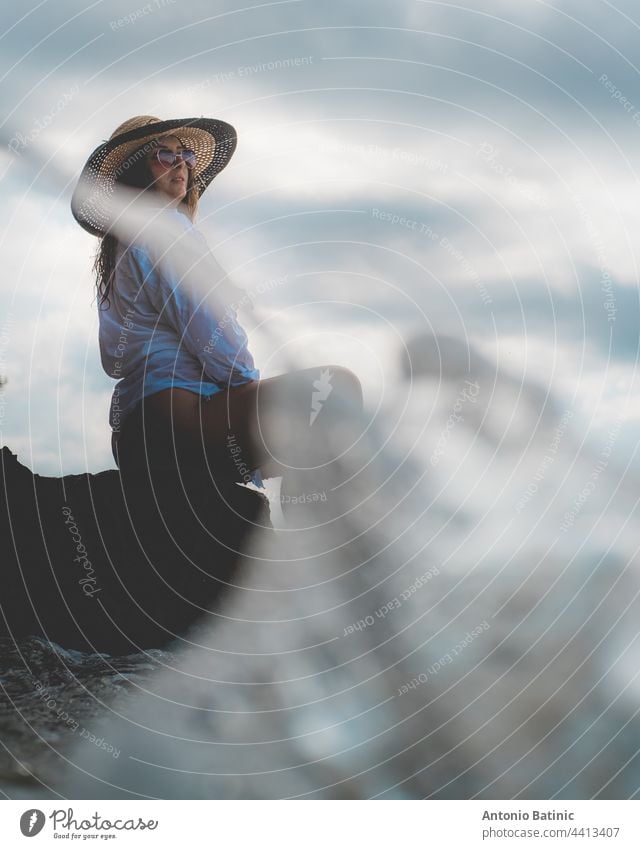 Side view of an amazing brunette sitting on a rock by the sea. Beautiful teal adriatic sea on the island of Vis, summer of 2021. Waves splashing on the shores