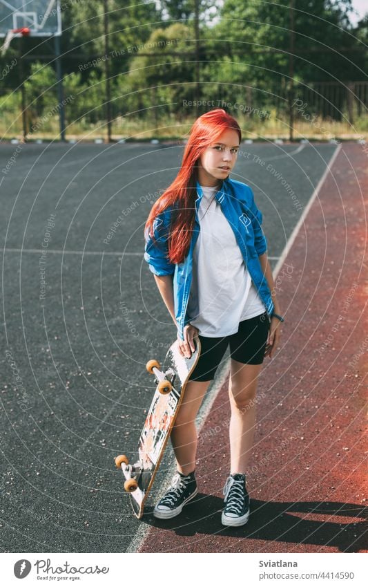 Portrait of a charming girl with a skateboard in her hand on a sports field sports ground street teenage hobby lifestyle young woman pretty outdoors modern