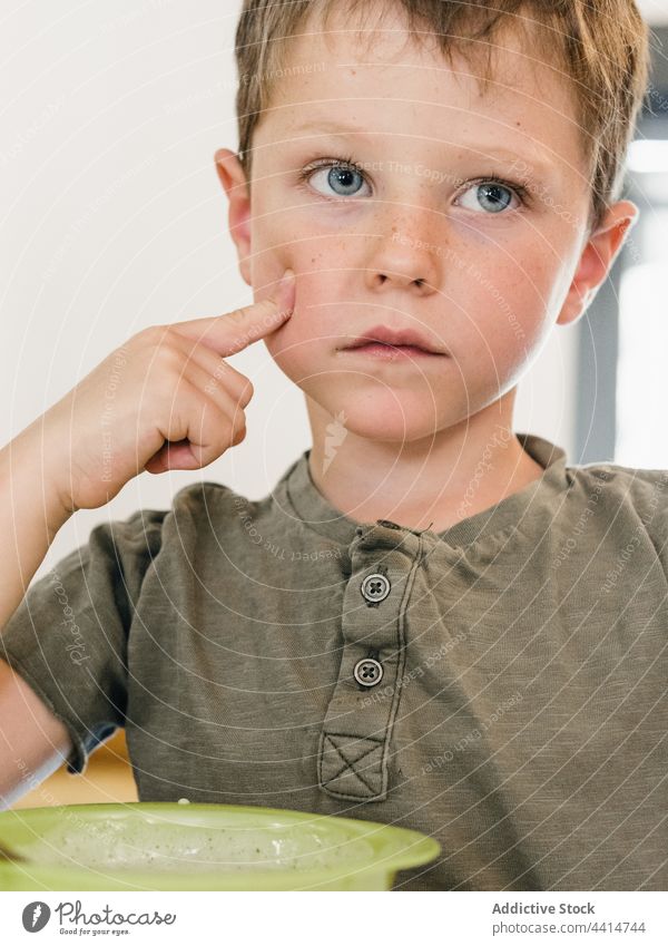 Cute boy sitting at table with food during lunch child adorable meal bowl kid home cute touch cheek sweet charming childhood tasty yummy delicious healthy dish