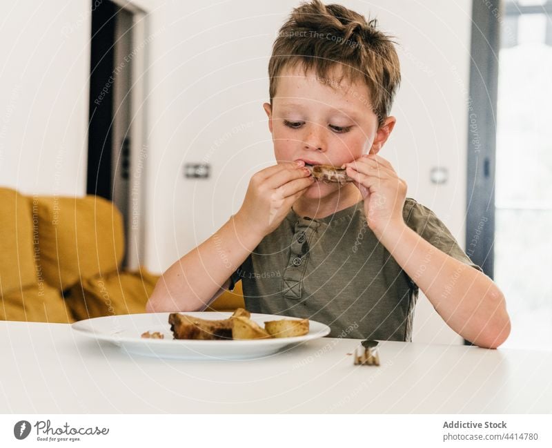 Hungry child eating pork ribs during lunch home food boy kid appetizing cute meal adorable enjoy tasty delicious nutrition domestic childhood homemade fresh