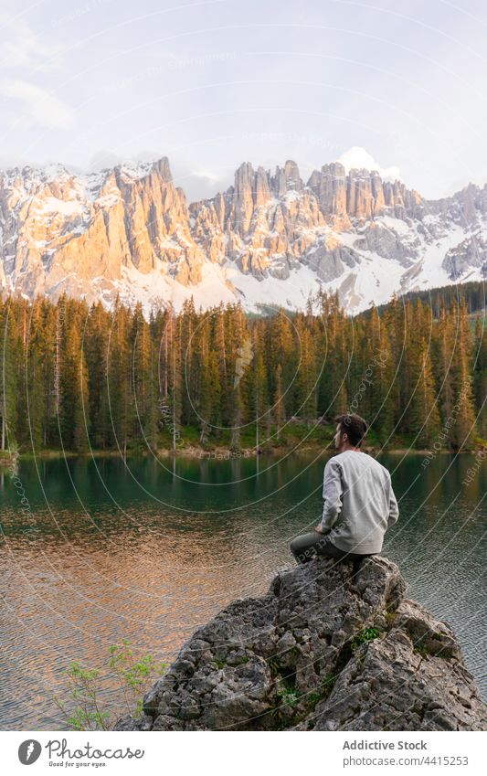 Traveling man sitting on rock near pond in mountains traveler lake admire highland sunset explorer male dolomite alps italy nature stone rocky range ridge