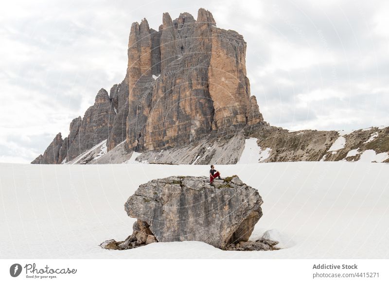 Traveler sitting on rock in mountains in winter traveler admire hiker highland snow trekking dolomite alps italy nature adventure weather explore explorer