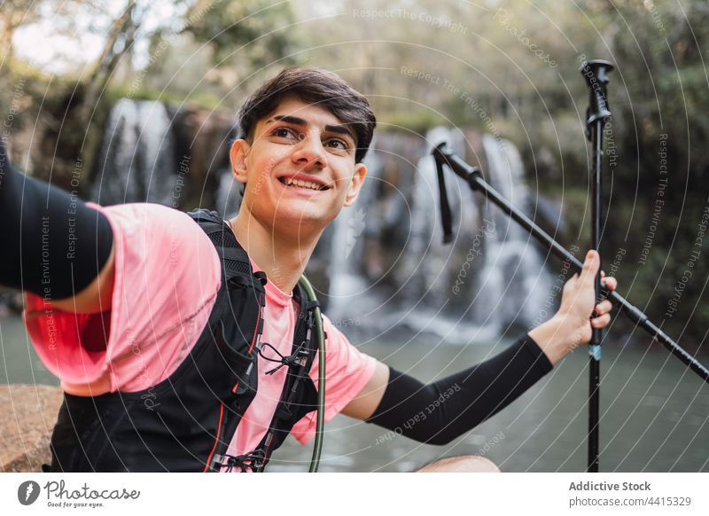 Traveling man taking selfie against waterfall in forest traveler smartphone self portrait hiker trekking memory male nature cheerful using take photo mobile