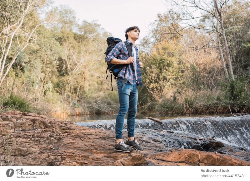 Traveling man standing near small waterfall in woods backpack forest hiker trekking traveler adventure male nature explore backpacker environment wanderlust