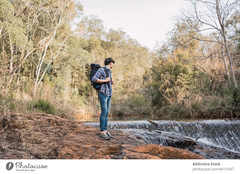 Traveling man standing near small waterfall in woods backpack forest hiker trekking traveler adventure male nature explore backpacker environment wanderlust