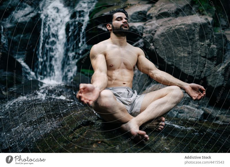 Serene man meditating in Lotus pose near waterfall meditate yoga lotus pose nature mudra zen padmasana mindfulness male harmony spirit tranquil serene practice