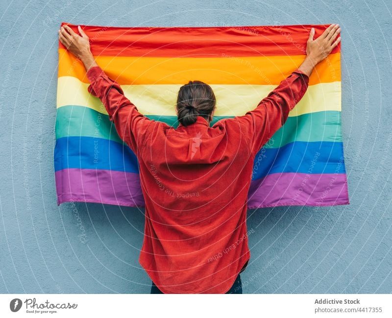 Unrecognizable gay man with rainbow flag near wall in city homosexual lgbt colorful pride lgbtq male equal tolerance street arms raised hand raised hand up