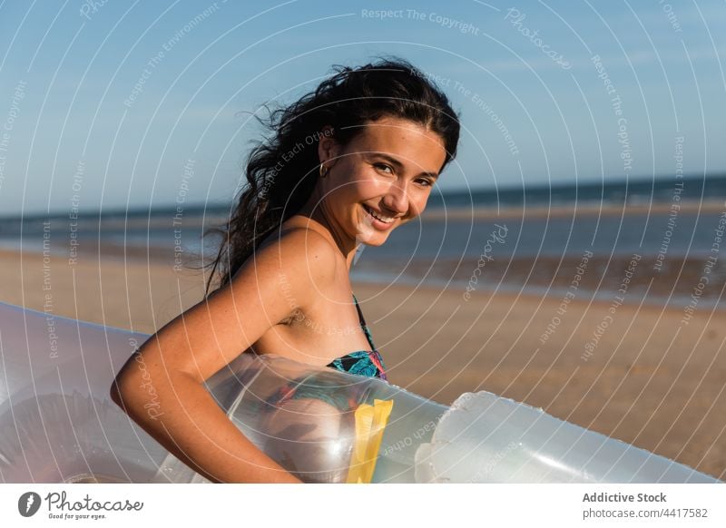 Cheerful woman walking along sandy beach in summer vacation sunny inflatable mattress smile female coast happy shore holiday sunshine blue sky cloudless sea