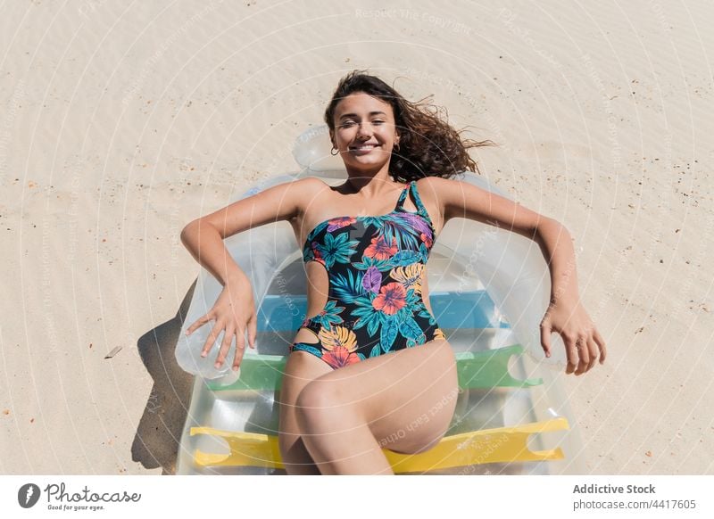 Cheerful woman sunbathing on inflatable mattress on beach suntan summer vacation swimsuit holiday female relax lying carefree pleasure sunlight summertime enjoy