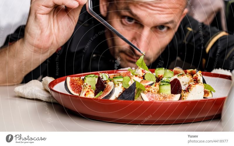 People at work. The chef prepares an tasty summer salad with ripe figs, goat chevre cheese, fresh cucumber roll, beetroot and mustard leaves with tomato sauce. Restaurant dish. Food banner