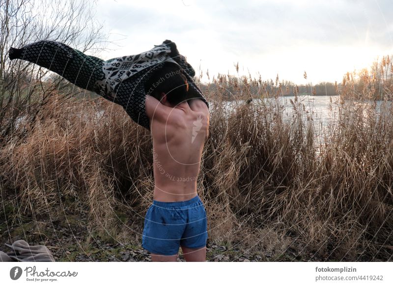 young man in winter landscape takes off his sweater - gets ready for ice bathing Ice bathing chill Cold Freeze Young man Man move out Extract Winter sports