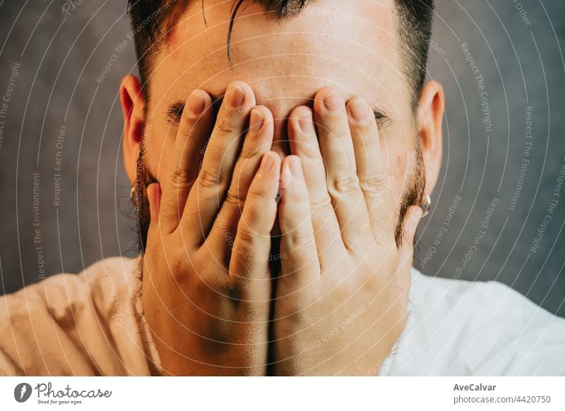 Super close up portrait of a Young bearded hipster man, yearning while touching his head with the hands and closing eyes mental health and depression advice