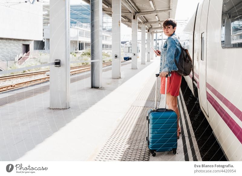 young backpacker caucasian woman holding luggage at train station ready to catch the train. Holding mobile phone while using app. Travel concept travel