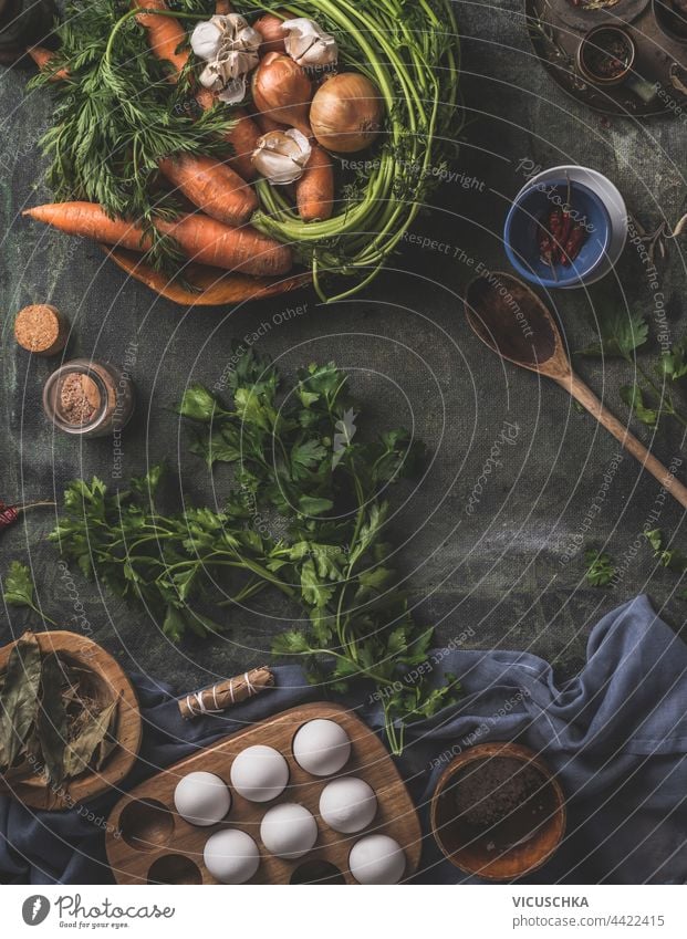 Healthy ingredients for tasty cooking at home. Fresh vegetables and herbs on a dark kitchen table with a wooden spoon, fresh eggs and dried seasonings . Top view