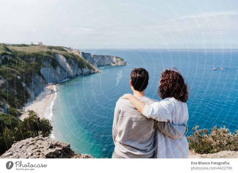 back view of two women friends relaxing and looking at beautiful sea landscape on top of the mountain. Friendship and nature concept couple cliff caucasian 30s