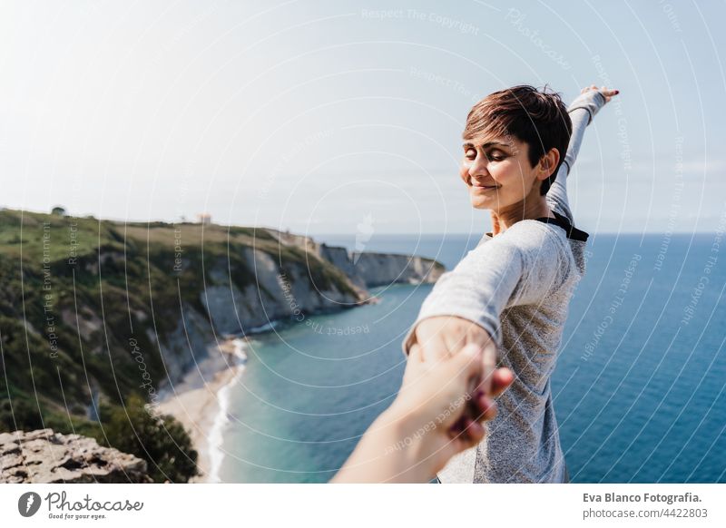 happy Girlfriend holding hand of boyfriend during hiking on top on the cliff. Sea view. Relax and nature concept woman relax enjoying back view young together