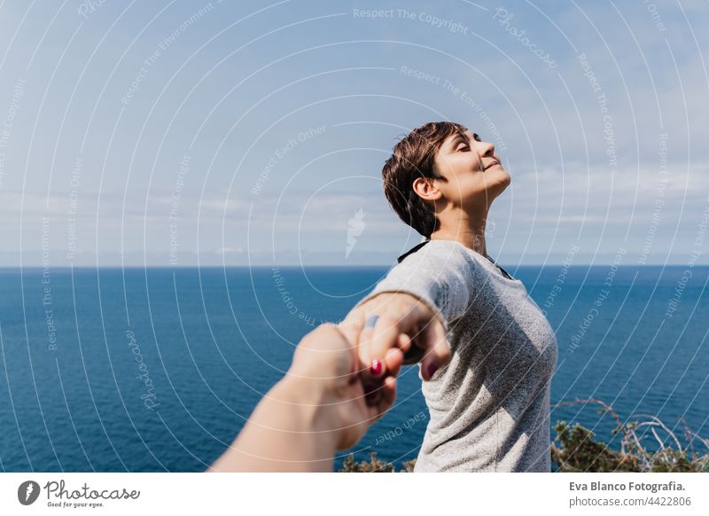 young smiling Girlfriend with eyes closed holding hand of boyfriend during hiking on top on the cliff. Sea view. Relax and nature concept woman relax enjoying