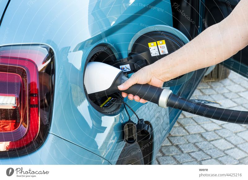 A woman's hand inserts a CCS charging plug into the connector of a blue electric vehicle CO²-neutrality electromobility Car Caucasian Charging plug Clean