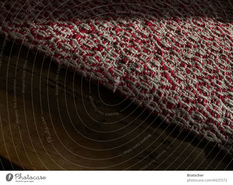 A traditionally handmade red and white tablecloth lies folded diagonally on an old, worn wooden table. Cloth Craft (trade) Table Woven weave Red White