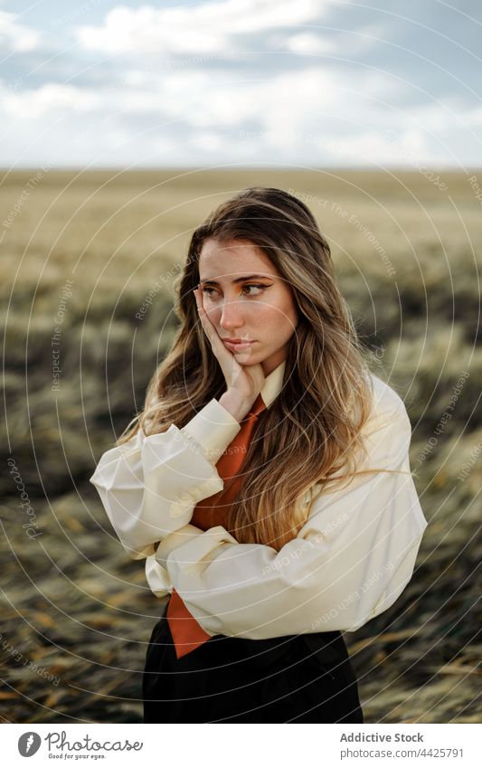 Bored woman in stylish wear in countryside field bored touch cheek style individuality apathy contemplate alone millennial farmland natural white shirt tie