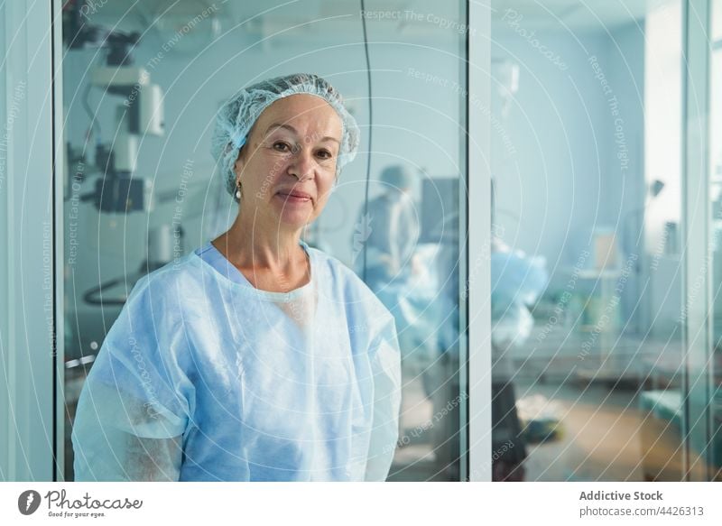 Smiling surgeon in medical uniform against glass wall in clinic doctor smile surgical friendly profession woman portrait hospital sincere professional sterile