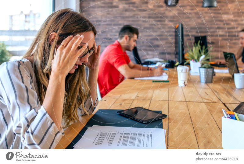 Stressed businesswoman with hands on head stressed at work burdened headache overworked work overload people lack of concentration caucasian pressure coworkers