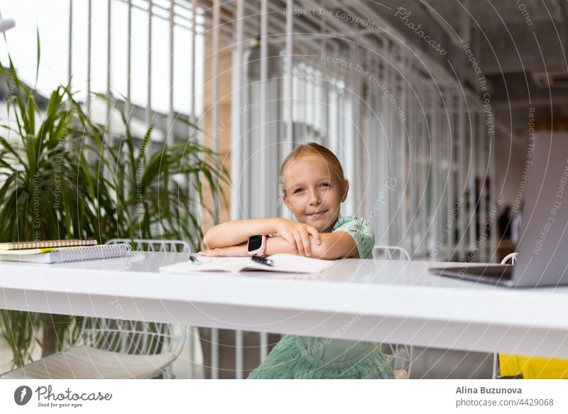 Back to school after summer vacations in new normal. Social distancing and Distance learning during quarantine shutdown. Lifestyle portrait of stylish Generation z girl seven years old wearing casual clothing, doing homework and using computer at cafe