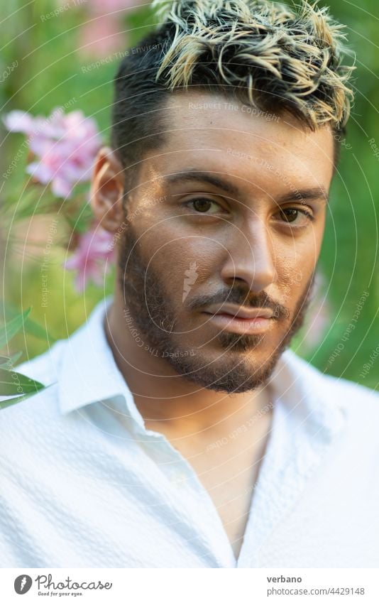 caucasian young man wearing white shirt in a park in summer with pink flowers and green leaves out of focus dancer gay happy lifestyle person pride background