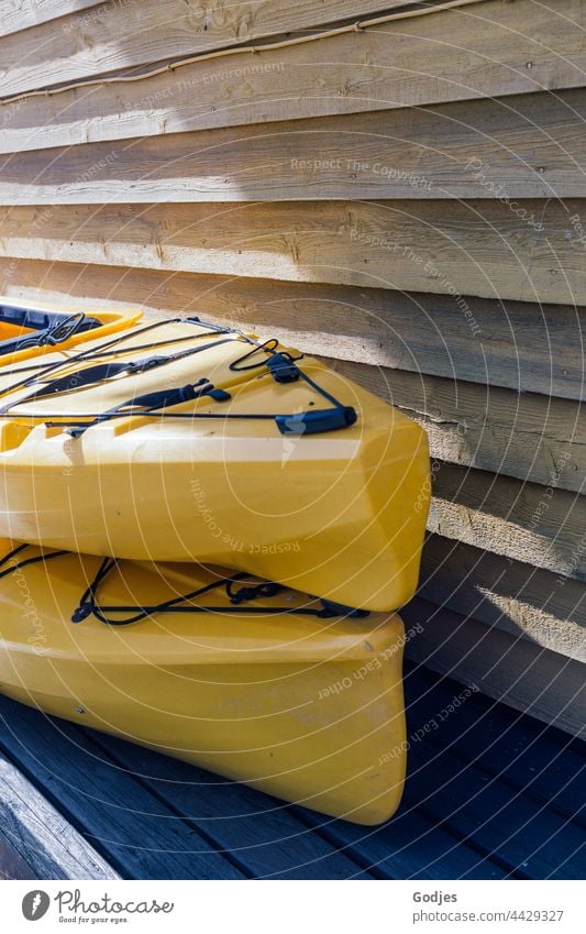 two yellow kayaks stacked next to a wooden wall Kayak Yellow Wooden wall plastic Colour photo Exterior shot Water Sports Aquatics Deserted Day Vacation & Travel