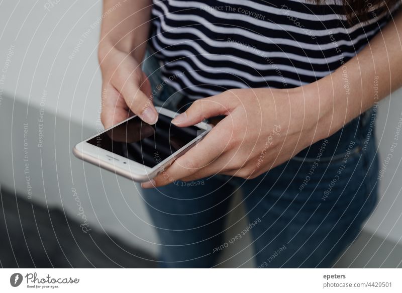 Young woman holding a smartphoneonly the hands are shown casual clothes gen z jeans striped stripes t-shirt tech technology unrecognizable using white young