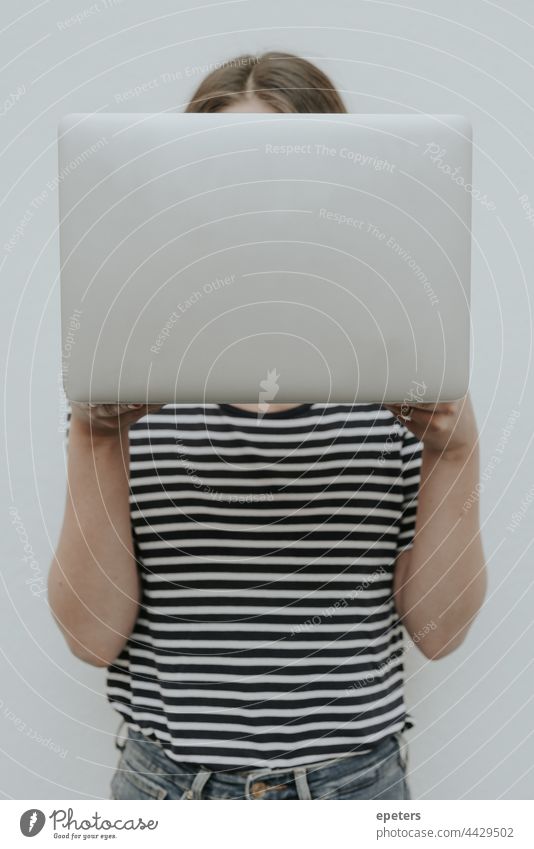 Young woman in jeans and t-shirt holds a silver laptop in front of her face Weapons brown hair Computer Self-confident Copy Space hide behind a computer