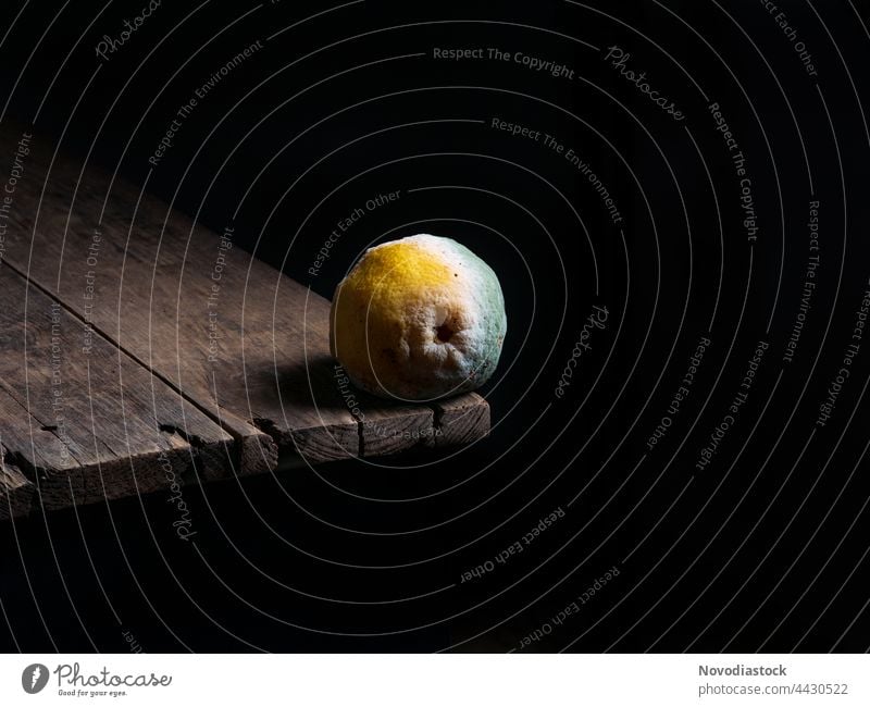 Rotten lemon on the edge of a wooden table, black background Lemon rotten fruit Fruit Yellow Citrus fruits Food Nutrition Healthy Vitamin Vitamin C Colour photo