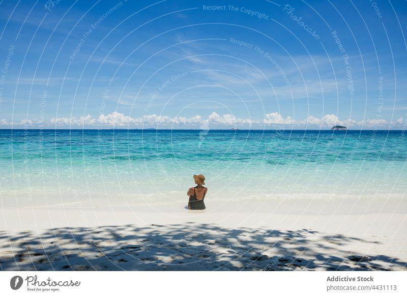 Woman sitting in clear sea woman tourist vacation holiday beach tropical trip turquoise travel female water traveler coast swimwear hat straw hat ripple shore