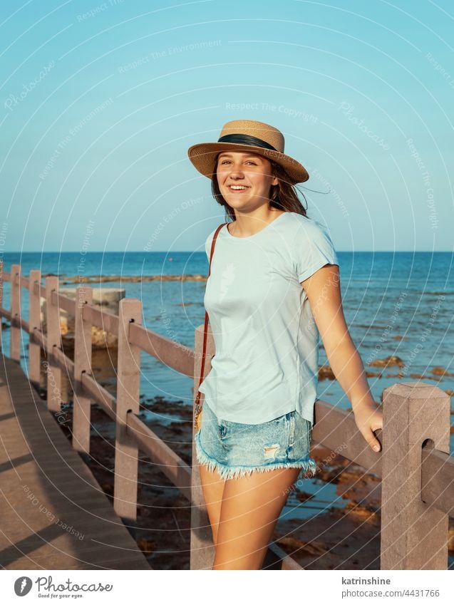 Teen girl standing on wooden bridge by the sea sunset teenager straw hat mockup Caucasian adolescent blue walkside sidewalk outdoor vacation travel look aside