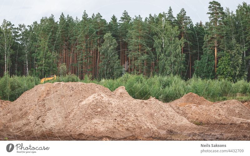 Industrial sand quarry. Sand pit. Construction industry. Sand hill against green forest and cloudy sky activity background blue building bulldozer business