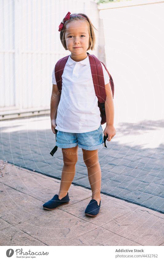 Schoolgirl in casual clothes with rucksack on urban walkway schoolgirl curious childhood back to school pavement stone wall charming dreamy tiled ribbed gentle