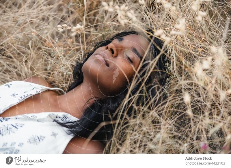 Concentrated Indian woman resting on faded grass in countryside eyes closed serene mindful harmony idyllic natural quiet mindfulness breath dry grow concentrate