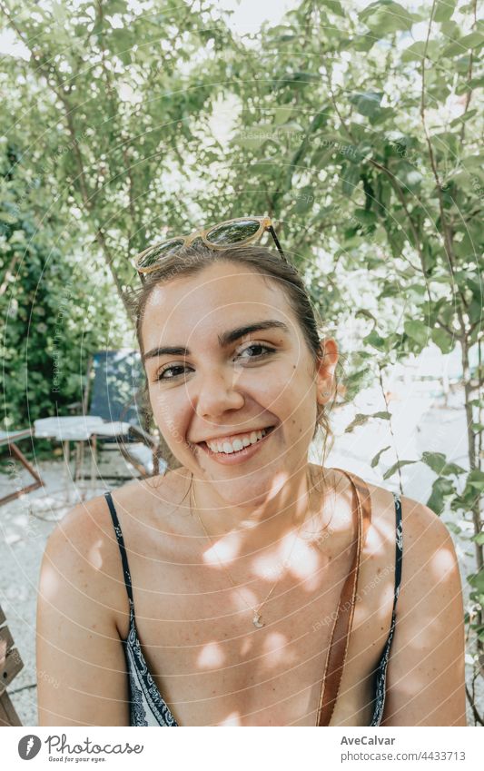 Close up portrait of a young woman smiling to camera while using sunglasses wearing a dress in a sunny garden businesswoman dentist front view horizontal