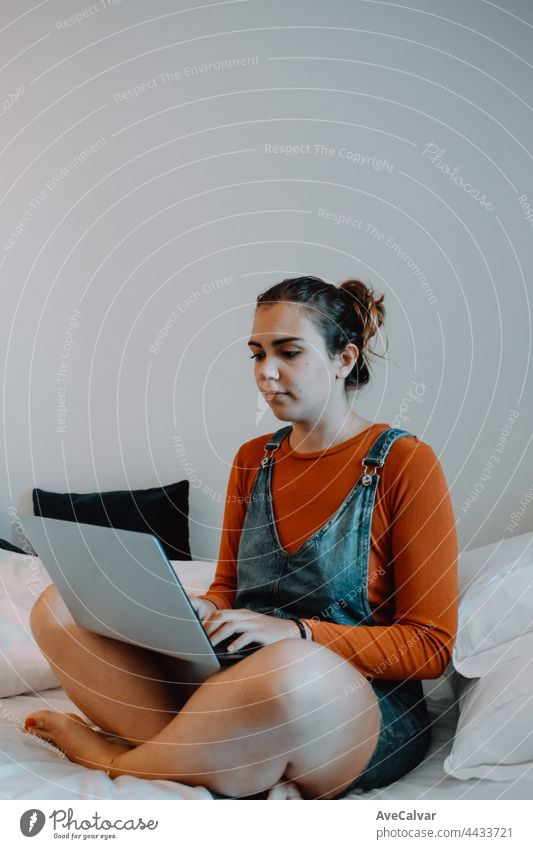 Young woman using his laptop while on bed, working from home, hipster style, minimal white house computer technology bedroom relaxation portrait emotion