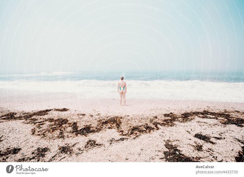 Small young woman in the middle of the beach during a sunny day, mental health concept, solitude fun swimwear emotion one person suit carefree sunbathing