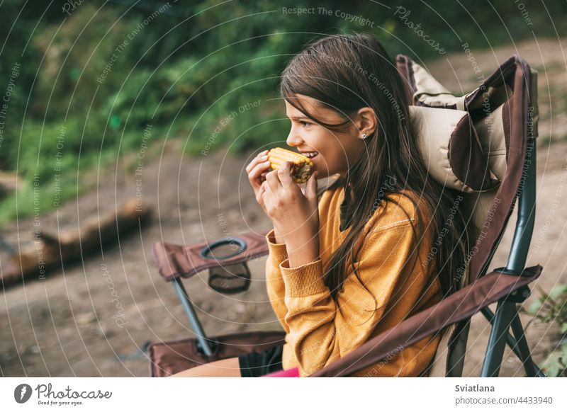 A teenage girl in a bright yellow sweater is sitting in a camping chair on the shore of the lake and eating corn woman nature female people vacation relaxation