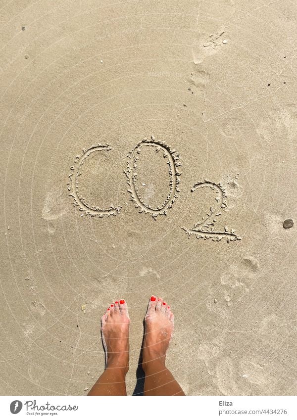 Feet in the sand in front of the word CO2 - Climate crisis and travel concept Sand co2 climate crisis Carbon dioxide CO2 emission vacation Beach Ocean co2 load