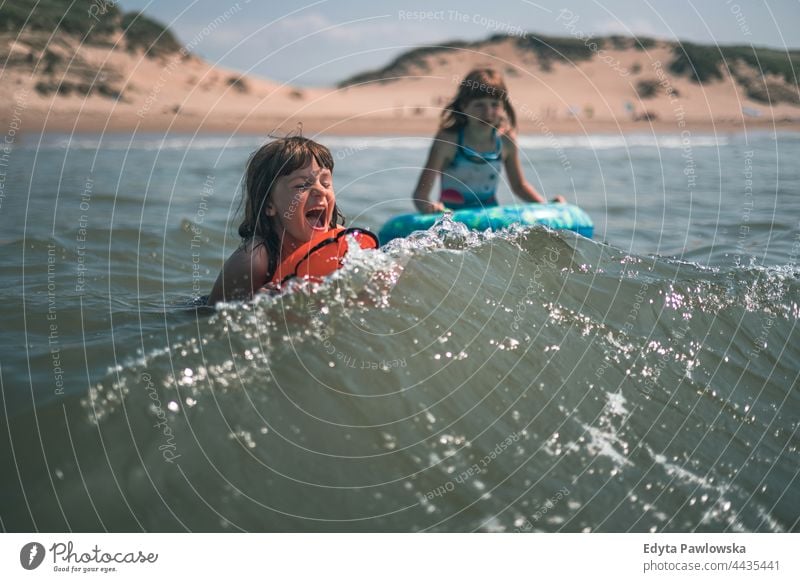 Two little girls swimming in the sea waves beach ocean sand sky water inflatable toy inflatable ring vacation travel active adventure summertime day freedom