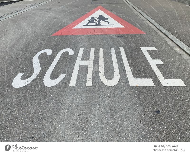 Warning sign of the way to school in German language  in Switzerland. Road sign is red triangle with running children in white field and text Schule, which means School.