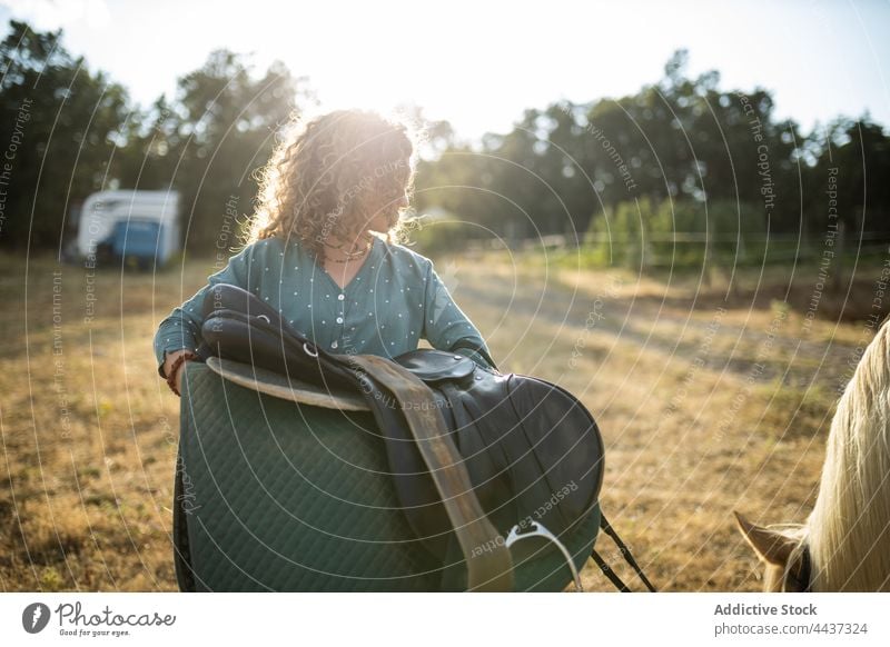 Woman with saddle against horse grazing on farm woman graze animal equine livestock domesticated riding school stallion fauna countryside mammal eat grass