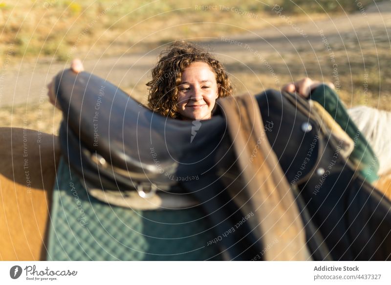 Woman putting saddle on back of horse in countryside woman mare prepare equine animal livestock domesticated farm riding school stallion fauna mammal equipment