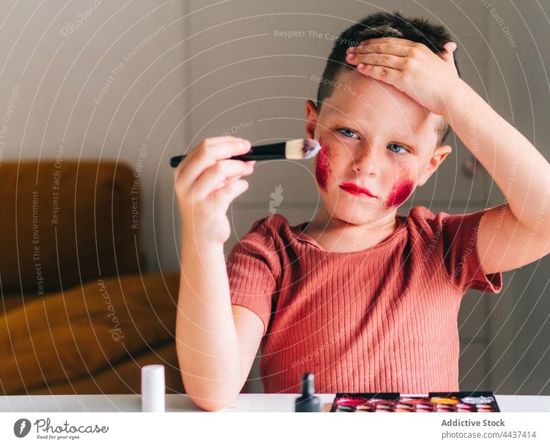 Boy applying makeup on face in house room boy applicator beauty cosmetic touch head decorative messy having fun portrait childhood palette product assorted