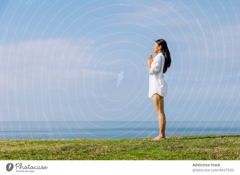 Asian woman with praying hands meditating on sea shore namaste meditate yoga spirit energy mindfulness vitality seashore sky cloudy asana asian ethnic