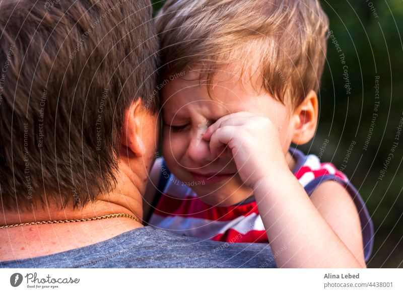 A little boy is crying while being in his father's arms, snuggling up to him to feel protected. expression caring relationship child son white parent sitting