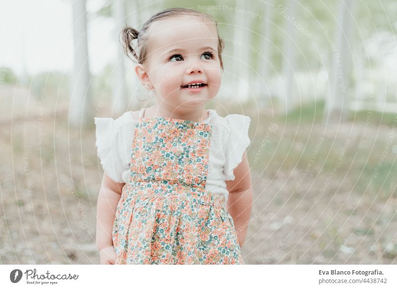 portrait of beautiful happy baby girl having fun outdoors in trees path. Children, fun and nature concept forest childhood smiling run caucasian Spain dress